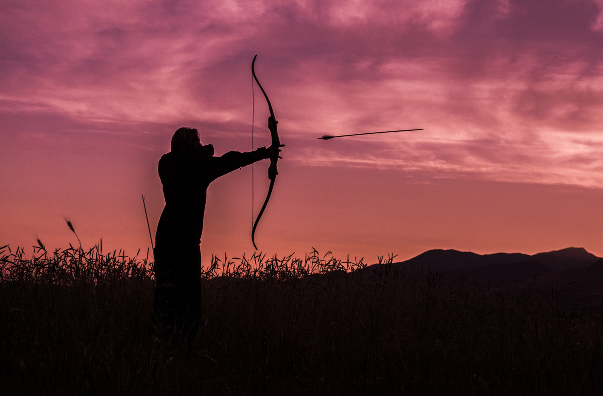person shooting an arrow silhouetted against the sky 