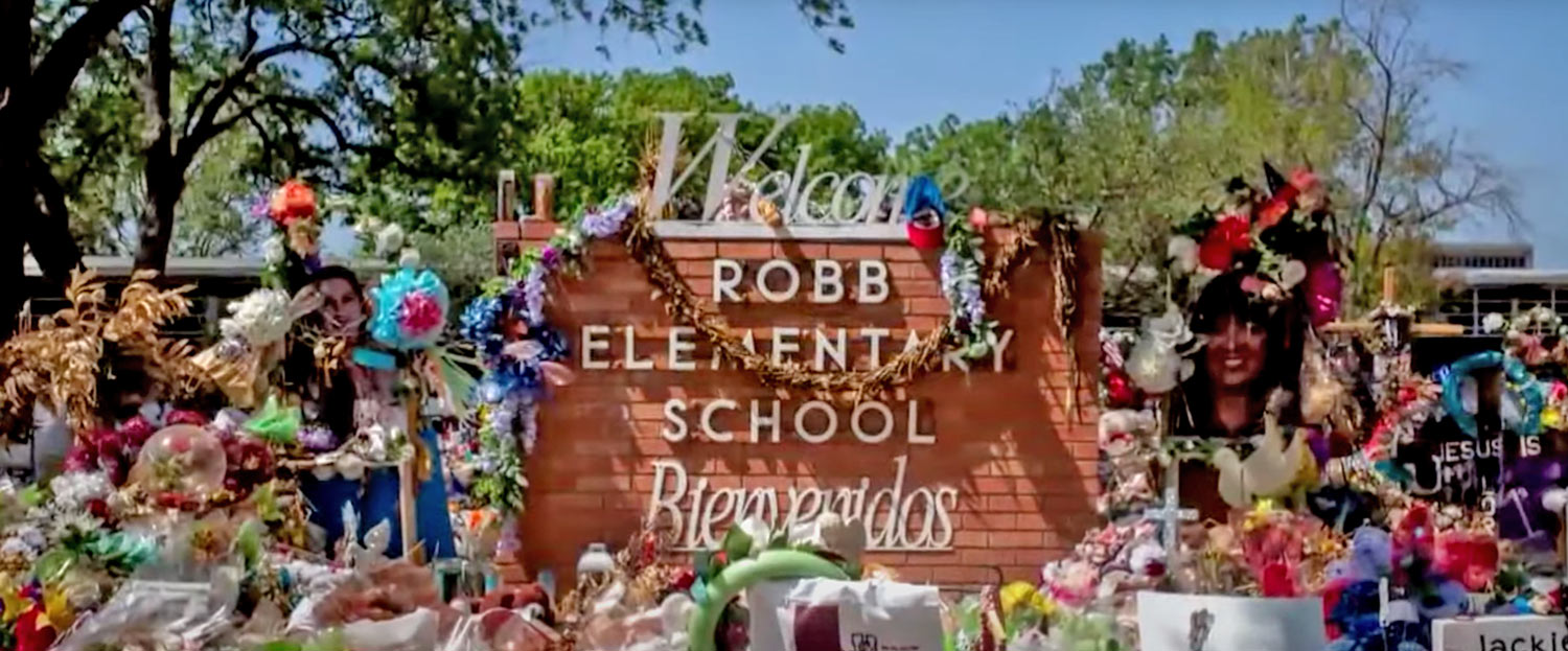Robb Elementary School signage surrounded by memorial wreaths, flowers and balloons