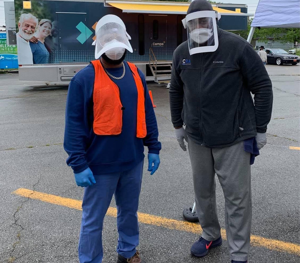 Community health advocates LaDarius Price and Chris Ramsey stand side by side wearing masks and plastic face shields while standing in a Chattanooga, Tennessee parking lot used for COVID testing