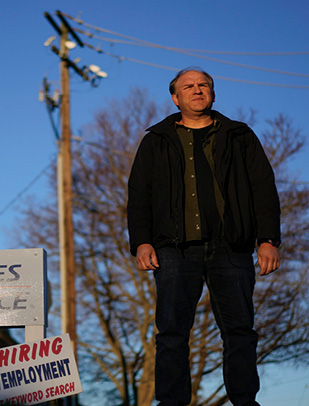 Man standing intently with electrical pole and what look like picketing signs in the background