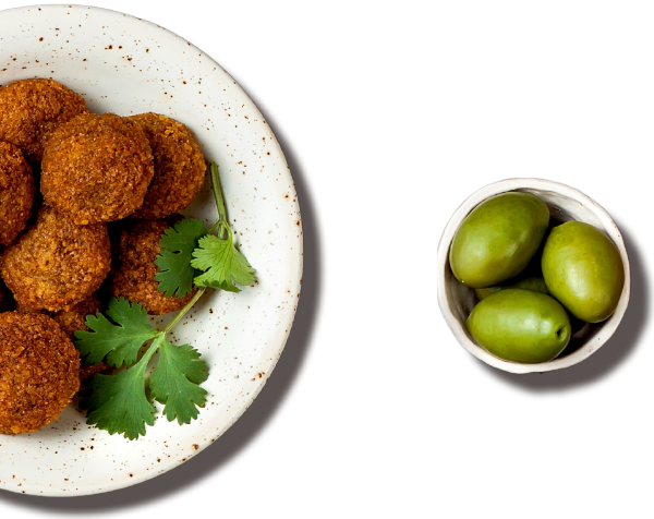 Falafel (deep-fried balls) with cilantro on a circular round plate and green olives in a small tiny round bowl
