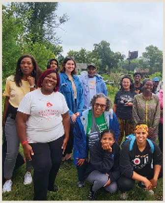 A group of diverse individuals posing outdoors in a grassy area, smiling and dressed in casual clothing, with trees and an overcast sky in the background.