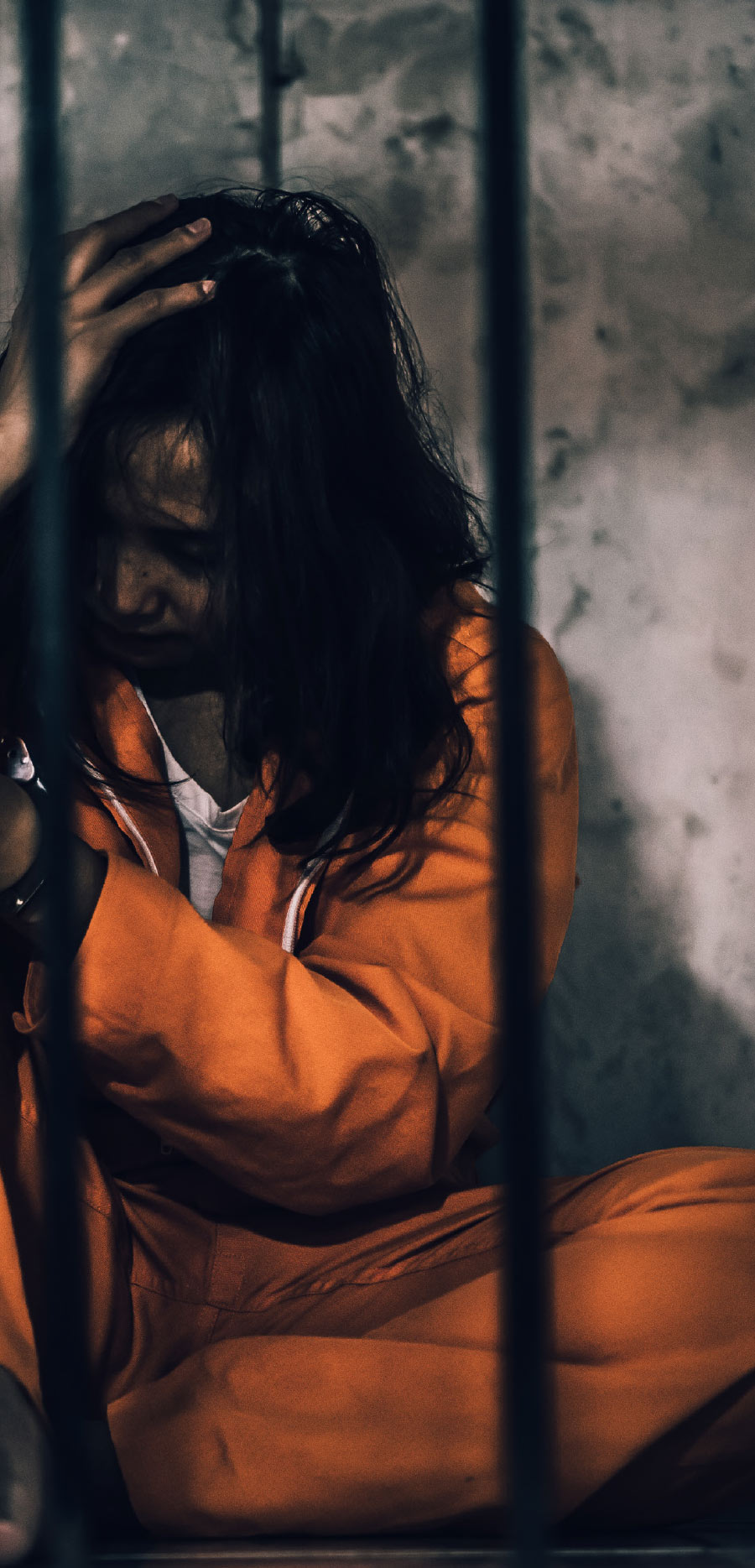 woman in orange jumpsuit behind bars with hands on head