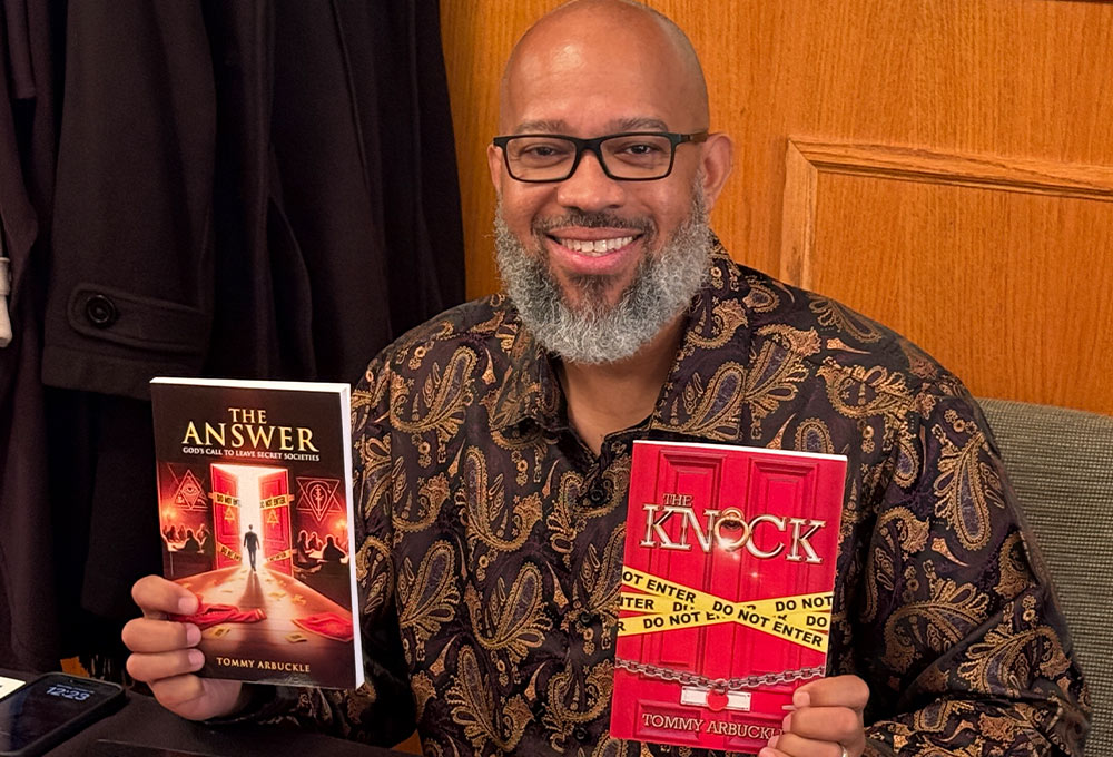 Tommy Arbuckle pictured seated and smiling while holding two of his books, The Answer and The Knock
