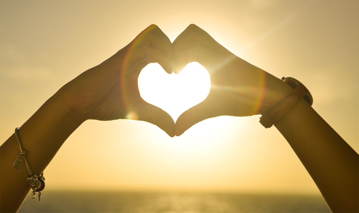 hands creating a heart shape with the sun shining through the middle