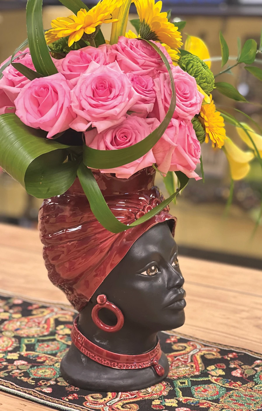 Ceramic head vase with pink roses, yellow flowers, and greenery on a patterned table runner.
