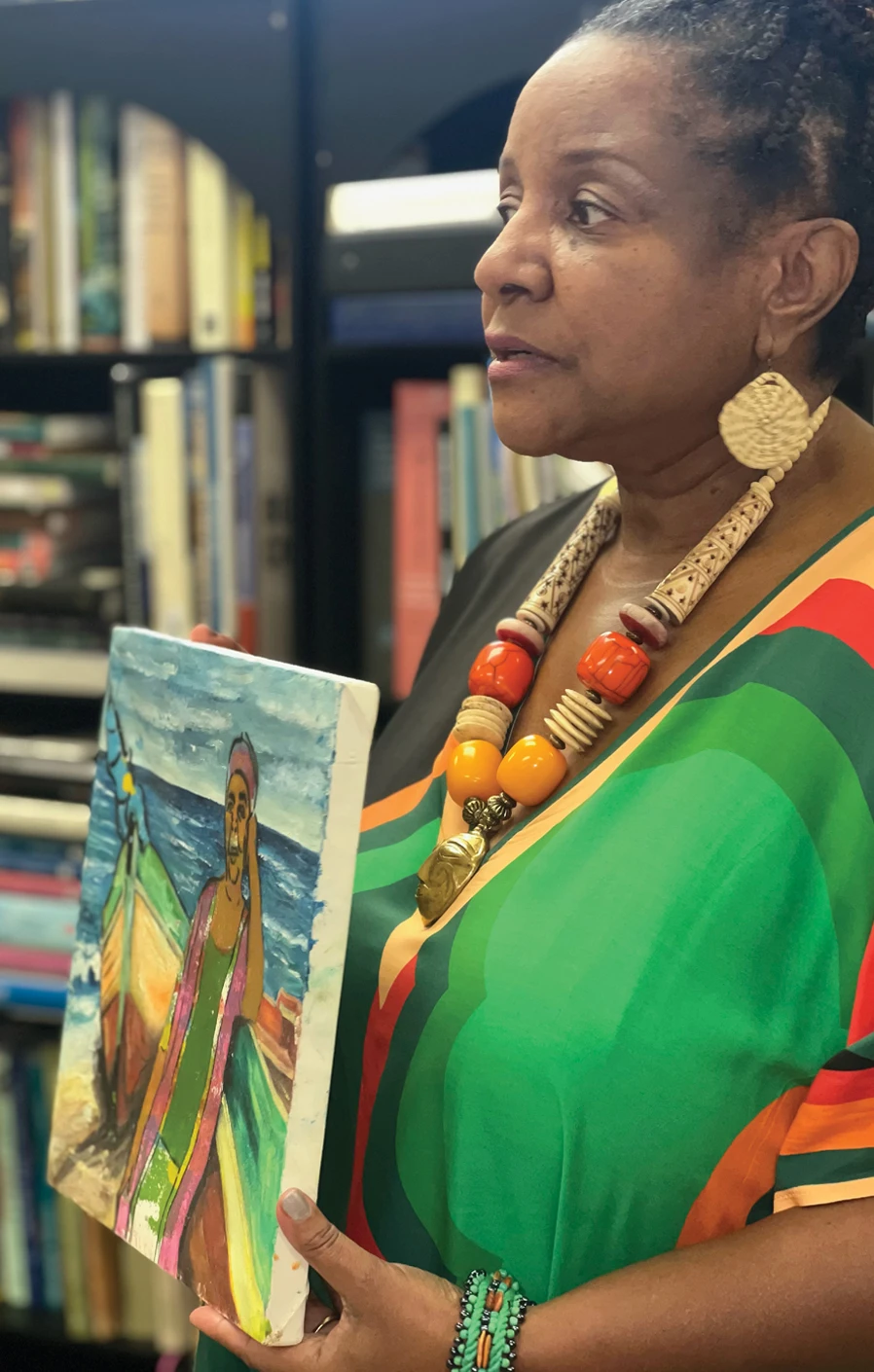 Woman holding a colorful painted portrait in front of bookshelves.