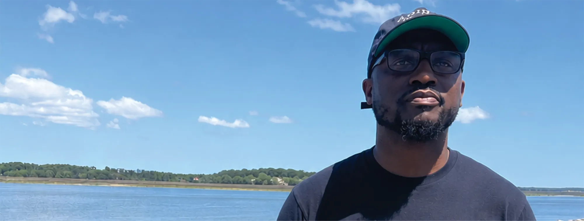 Man standing near the water under a bright blue sky.