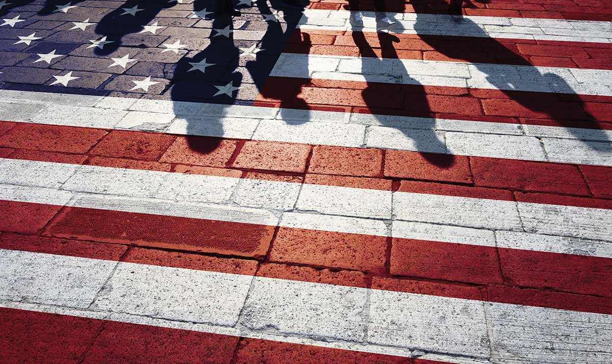 The shadows of several people cast onto a brick path painted with the American flag.