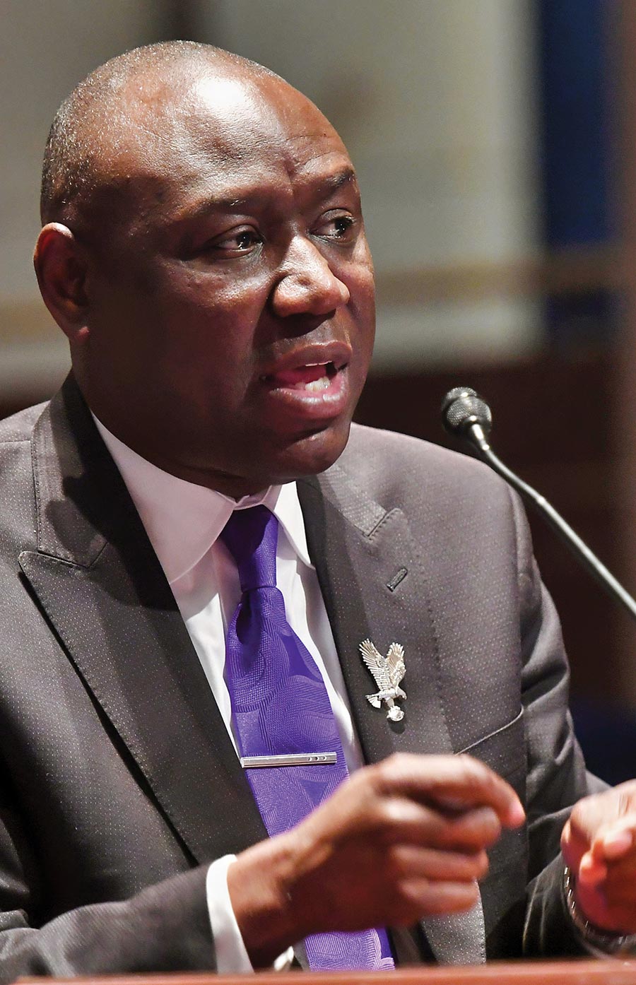 Attorney Ben Crump speaking into a microphone while wearing a suit and purple tie.