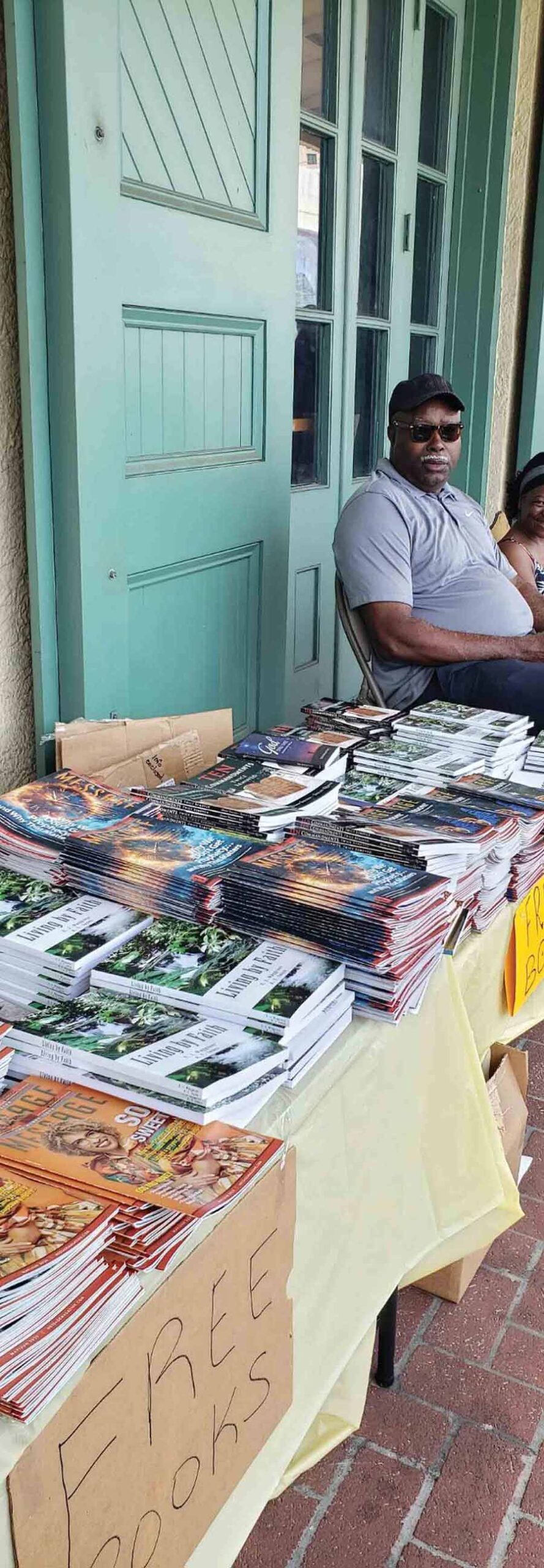 Man sitting beside outdoor tables stacked with free books and magazines for distribution.